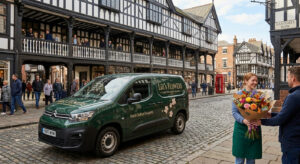 A Lili's Flowers delivery van parked on the historic cobbled streets of Chester near Eastgate Row, with a florist hand-delivering a vibrant bouquet of fresh flowers to a customer.