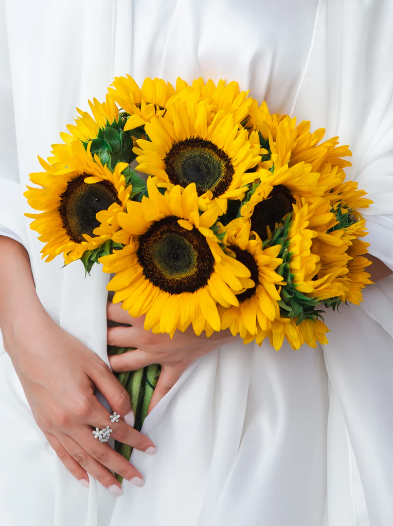 Graduate in a white dress holding a vibrant bouquet of bright yellow Graduation Day Flowers